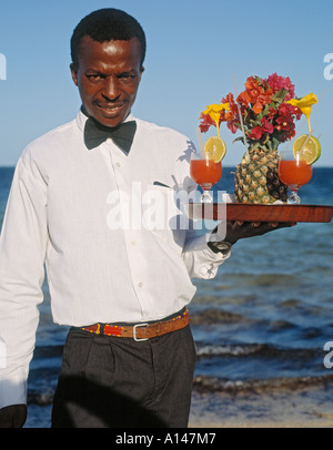 Mombasa, in Kenya. Africano nero cameriere con vassoio di drink esotici e l'oceano dietro. Foto Stock