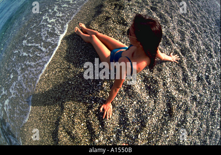 Vista aerea di una donna che indossa gli occhiali da sole e un bikini costume da bagno seduta sul bordo dell'acqua su una grossa spiaggia di sabbia Foto Stock