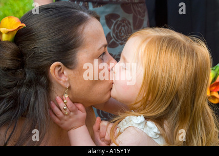 Chiudere orizzontale su ritratto di una madre e figlia giovane (Chief damigella e flowergirl) avente un bacio al sole. Foto Stock