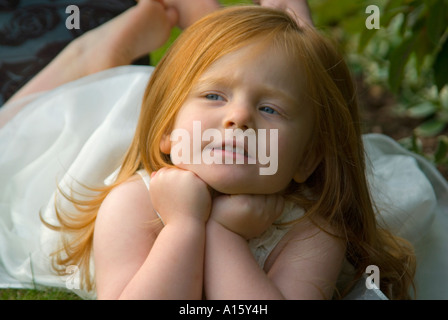 Chiudere orizzontale su ritratto di una giovane angelico flowergirl appoggiato il suo mento sulla sua mano mentre sdraiati sull'erba a un matrimonio Foto Stock