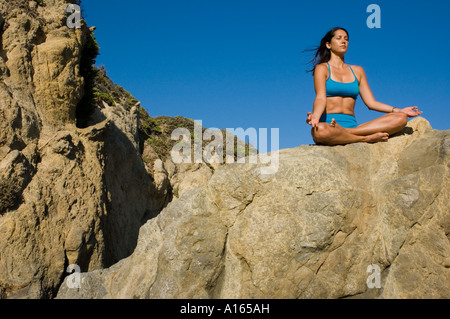 Giovane donna a praticare yoga sulla spiaggia rocciosa e meditazione Foto Stock