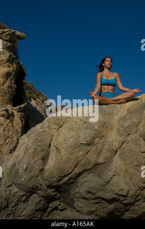 Giovane donna a praticare yoga sulla spiaggia rocciosa e meditazione Foto Stock