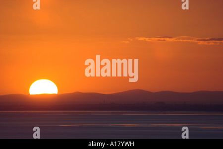 horizontal landscape photo of sunset as the sun dips behind the hills of the isle of man over morecambe bay Foto Stock