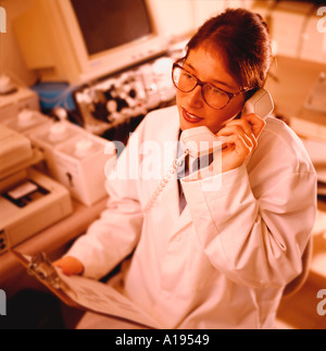 Femmina tecnico di laboratorio a parlare al telefono mentre si sta guardando un clipboard Foto Stock