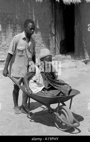 B/N di un ragazzo che porta la sua nonna anziana al mercato del villaggio in una carriola, vicino a Zaka, Zimbabwe. Foto Stock