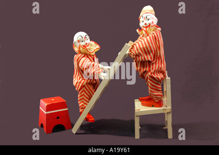 Due antiche in legno circus clown giocattolo in piedi su una sedia e la scaletta Foto Stock