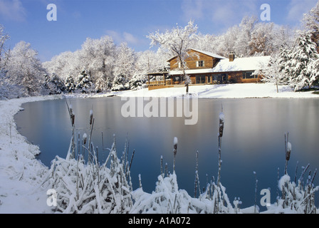 Grazioso a due piani di legno di cedro country house con grande terrazza vista attraverso un laghetto congelato in un nevoso inverno smerigliato giorno, Missouri USA Foto Stock