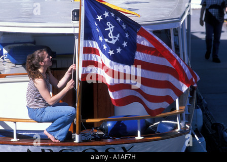 Stati Uniti Washington Seattle giovane donna si siede da bandiera sulla poppa di classic yacht in legno nel centro barca dock Foto Stock