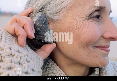 Donna senior in possesso di una shell per l'orecchio Foto Stock