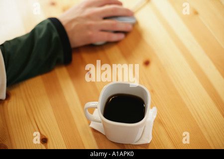Mano sul mouse del computer con la tazza di caffè Foto Stock