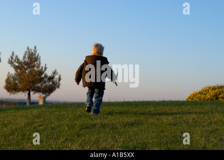 Un piccolo ragazzo di scappare dalla fotocamera con un piano giocattolo in mano Foto Stock