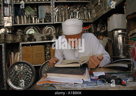 Negoziante la lettura del testo sacro dell'Islam Corano in Khan el-Khalili un grande souk nel centro storico del Cairo islamico Egitto Foto Stock