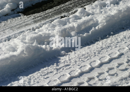 Tyre tire tracks in thawing melting snow on tarmac asphalt road in County Antrim Northern Ireland Foto Stock