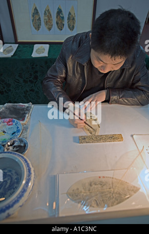 Cina CHONGQUING artista cinese utilizzando inchiostro e spazzola per dipingere scene tradizionali su foglie Foto Stock