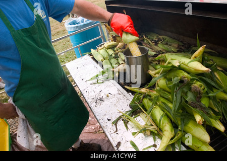 Fornitore maschio ad una fiera in Connecticut USA immergendo una spiga di grano in un contenitore di burro fuso che è accanto a un mucchio di roa Foto Stock