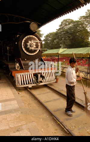 Una locomotiva a vapore nera d'epoca parcheggiata su una piattaforma della stazione con un uomo che spazza il terreno nelle vicinanze sotto un tetto riparato. Foto Stock
