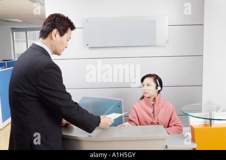 Il profilo laterale di un imprenditore in piedi in un ufficio a parlare con la persona addetta alla reception Foto Stock