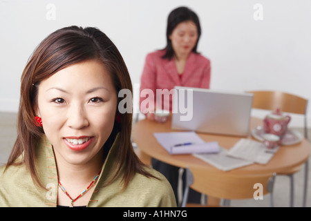 Ritratto di una imprenditrice sorridente con un'altra imprenditrice usando un computer portatile dietro di lei Foto Stock