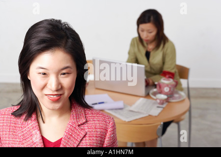 Ritratto di una imprenditrice sorridente con un'altra imprenditrice usando un computer portatile dietro di lei Foto Stock