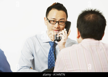 Ritratto di un imprenditore parlando al telefono con due imprenditori seduto di fronte a lui Foto Stock