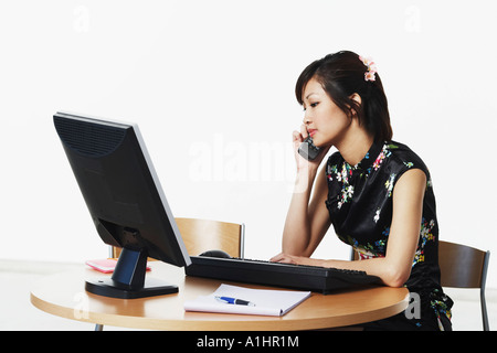 Giovane donna seduta di fronte a un computer parlando al telefono Foto Stock