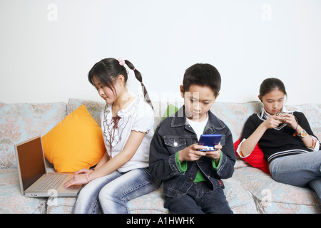 Ragazzo seduto su un divano la riproduzione di un video gioco accanto ai suoi due sorelle Foto Stock