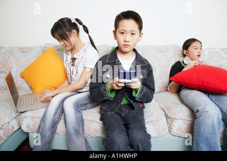 Ritratto di un ragazzo la riproduzione di un video gioco accanto ai suoi due sorelle Foto Stock