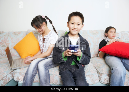 Ritratto di un ragazzo la riproduzione di un video gioco accanto ai suoi due sorelle Foto Stock