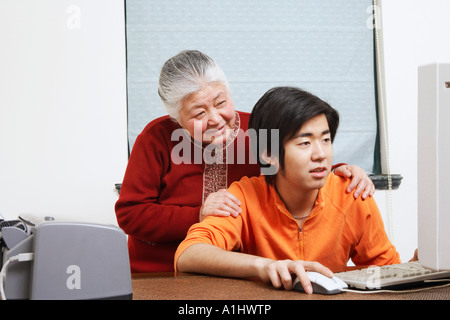 Close-up di un nipote utilizzando un computer con sua nonna dietro di lui Foto Stock