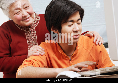 Close-up di un nipote utilizzando un computer con sua nonna dietro di lui Foto Stock