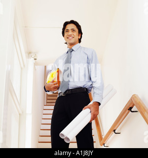 Basso angolo di vista di un architetto maschio holding arrotolato blueprint e un hardhat Foto Stock