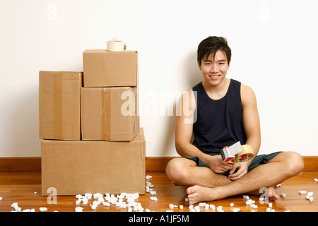 Ritratto di un giovane uomo seduto sul pavimento e tenendo un distributore di nastro Foto Stock