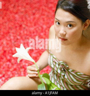 Angolo di alta vista di una giovane donna tenendo un fiore e seduto vicino a una vasca calda riempita con petali di rosa Foto Stock