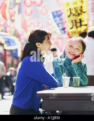 Giovane donna a parlare su un telefono mobile seduta con un altro giovane donna in un ristorante Foto Stock