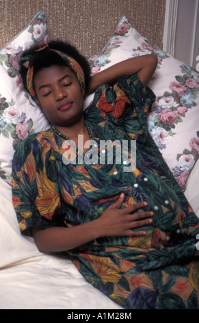 Nero/donna africana in gravidanza tardiva sdraiato sul divano con il resto Foto Stock