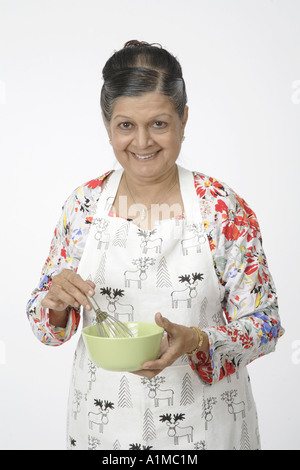 Indian senior citizen con utensili da cucina che indossa il grembiule per cucinare Foto Stock