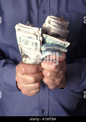 Business uomo clenched pugno che afferra e tenendo su pile di contanti assortiti in sterlina banconote in banca posti dal modello Inghilterra UK Foto Stock