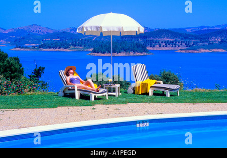 Donna godendo il sole presso la piscina della Pousada de Santa Clara Barragem de Santa Clara Alentejo Portogallo Foto Stock