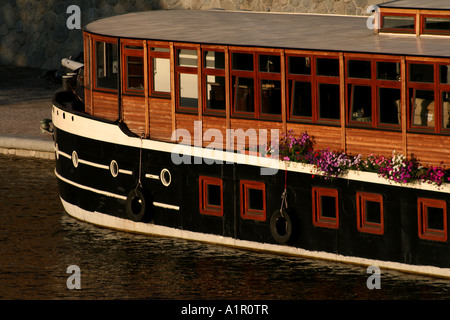 Affascinante casa galleggiante con fiori ormeggiati sul fiume, che mostra uno spazio unico e pittoresco sull'acqua. Foto Stock