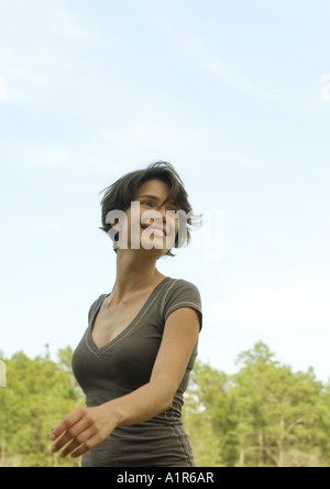 Donna passeggiate all'aperto, sorridente, alberi in background Foto Stock