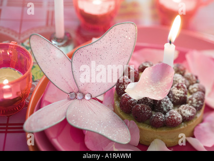 Lampone tartlet su lastra decorata con candela, farfalle e petali di rosa Foto Stock