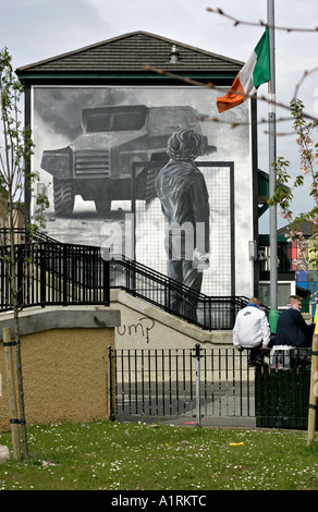 In attesa accanto alla sommossa. Un gruppo di ragazzi che si siede su una parete di fronte al murale bogside La Rioter un repubblicano irlandese bandiera vola Foto Stock