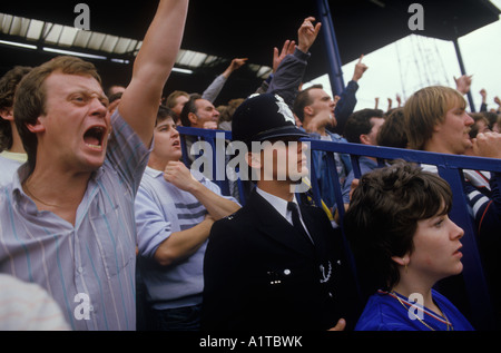 I tifosi del Chelsea Football Club degli anni '1980 gridano supporto per la loro squadra, lo Stamford Bridge London. Agente di polizia in servizio che si gode la partita 1985 UK Foto Stock
