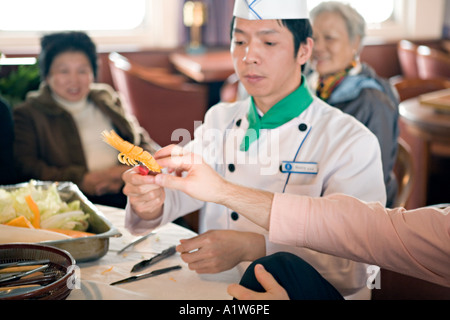 Cina fiume Yangtze Chef dimostra la tecnica di intaglio vegetali da intagliare una carota per assomigliare ad un gambero Foto Stock