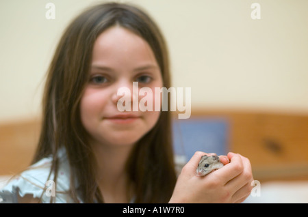 Nove anni di bambina gioca con pet hamster a casa in camera da letto guardando nella telecamera Foto Stock