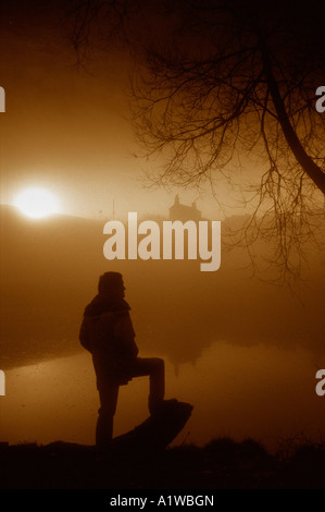 Profilarsi la figura di un uomo,guardare il sole sorgere attraverso una nebbia atmosferica paesaggio Staffordshire. Foto Stock