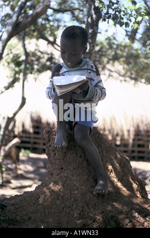 Biddi Biddi scuola Uganda un giovane bambino studiando, seduti su una formica/termite hill Foto Stock