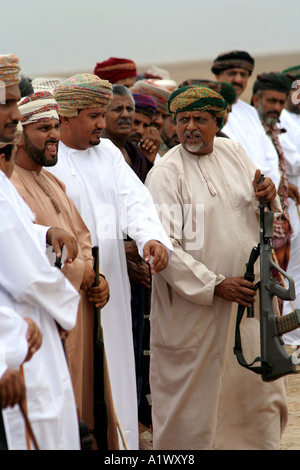 Gli uomini con spade e fucili in un cerchio, uno con un sistema automatico di fucile d assalto a una celebrazione, Salalah, Oman Foto Stock