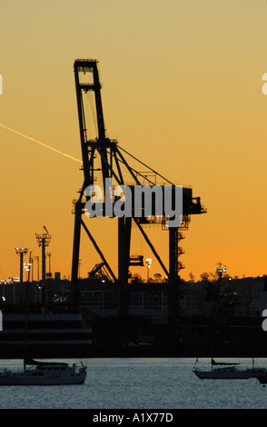 Un contenitore di spedizione gru in silhouette contro il tramonto porti di Auckland container terminal Nuova Zelanda Foto Stock