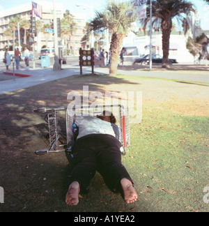 Una povera donna senzatetto piedi sporchi addormentato con la sua testa in un carrello di shopping in Santa Monica park a Los Angeles California USA US KATHY DEWITT Foto Stock